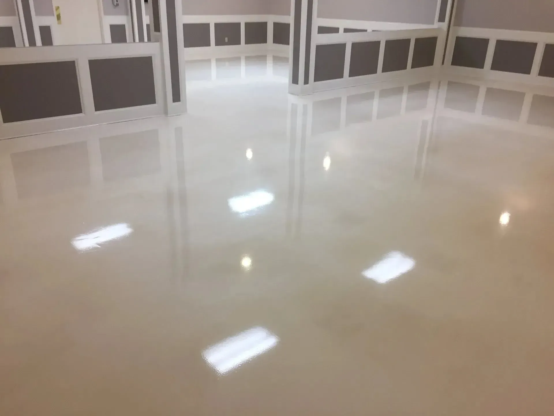 Shiny, light-colored floor reflecting overhead lights in a room with white walls and dark trim.