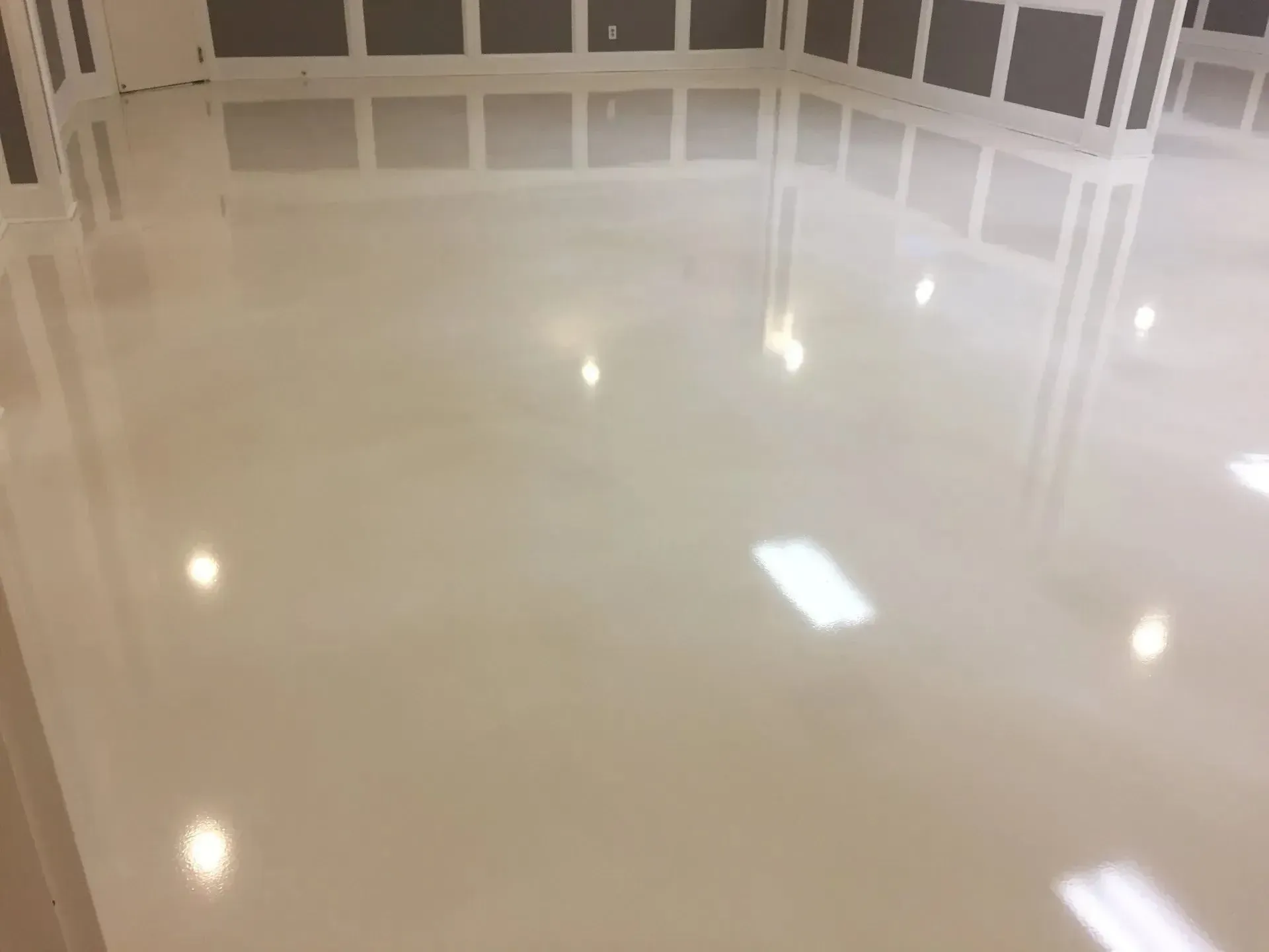 Glossy, light-colored epoxy floor reflecting ceiling lights in a room with a decorated wall.