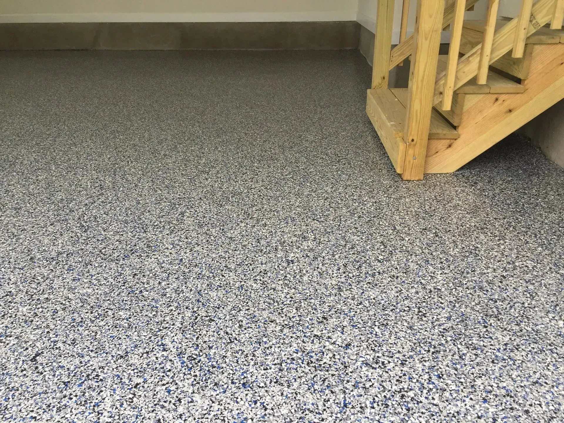 Garage floor with speckled epoxy coating. Stairs with wooden railing on the right.