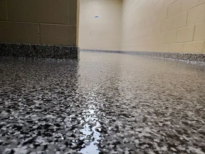 Close-up of a shiny, speckled epoxy floor in a hallway with tan brick walls and baseboard.