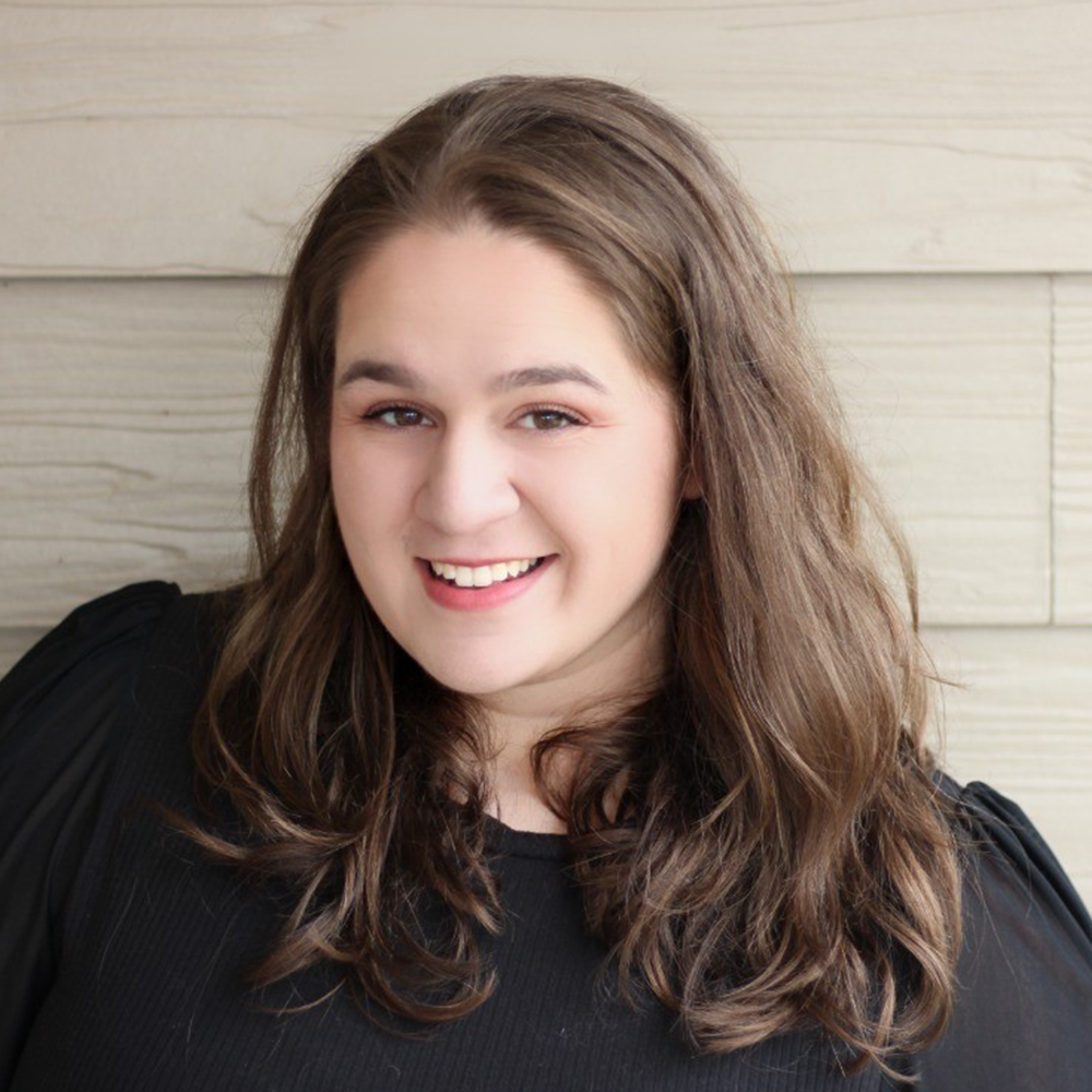 A woman with long brown hair is smiling and wearing a black shirt