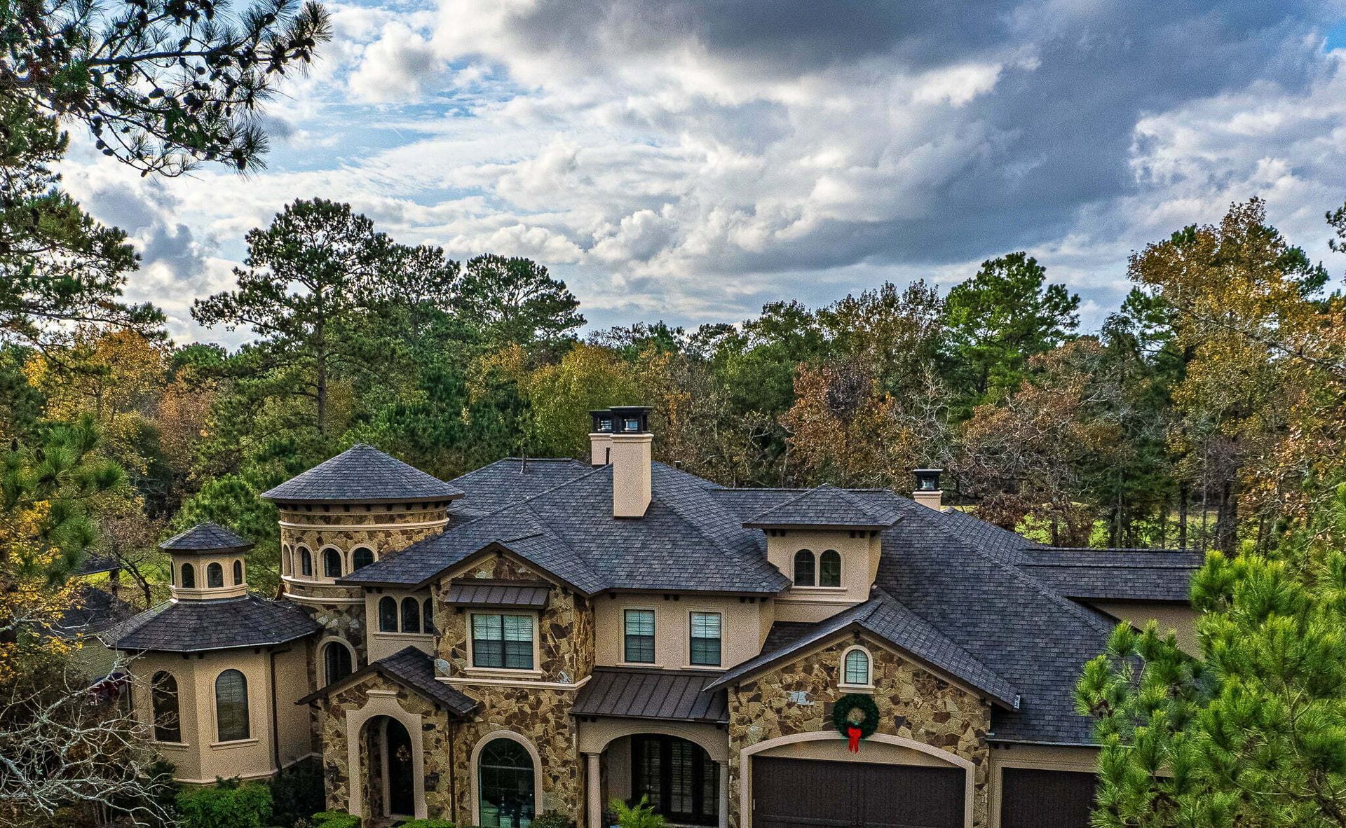 A large house is surrounded by trees and a cloudy sky.