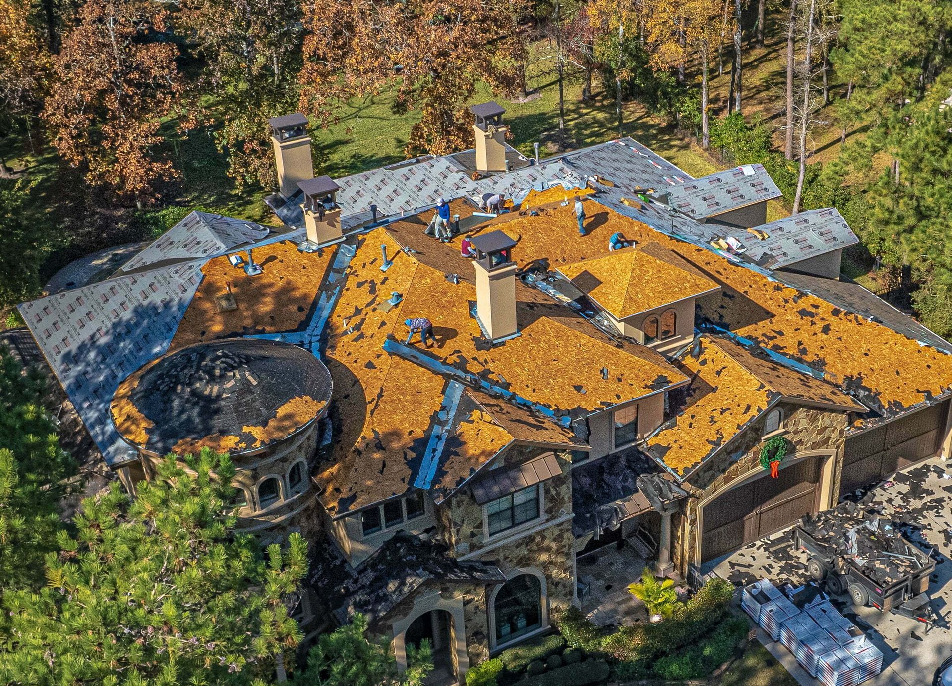 An aerial view of a large house with a roof in the middle of a forest.