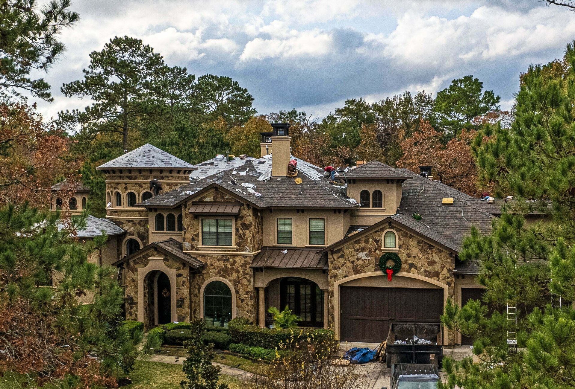 A large house with a wreath on the garage door is surrounded by trees.