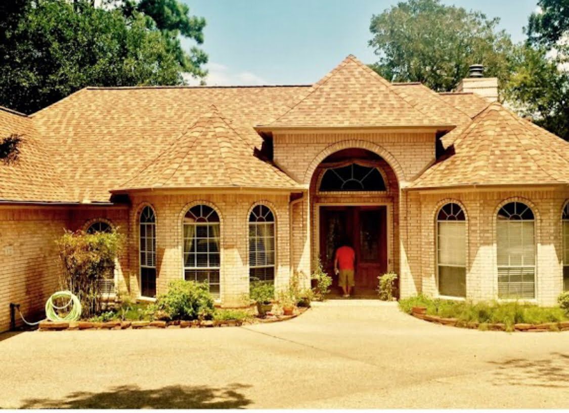 A man in a red shirt is standing in front of a large brick house.