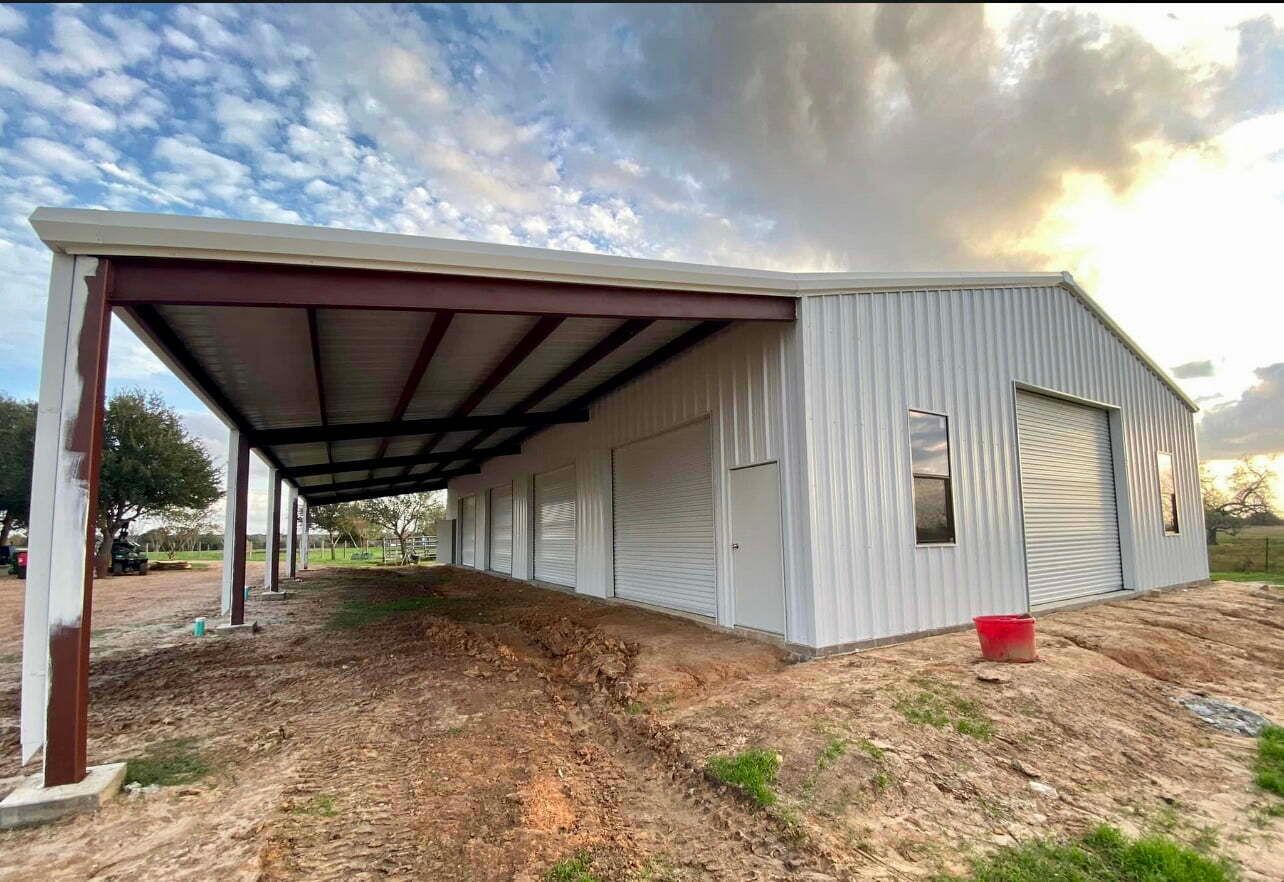 A white metal building with a canopy over it is sitting on top of a dirt field.