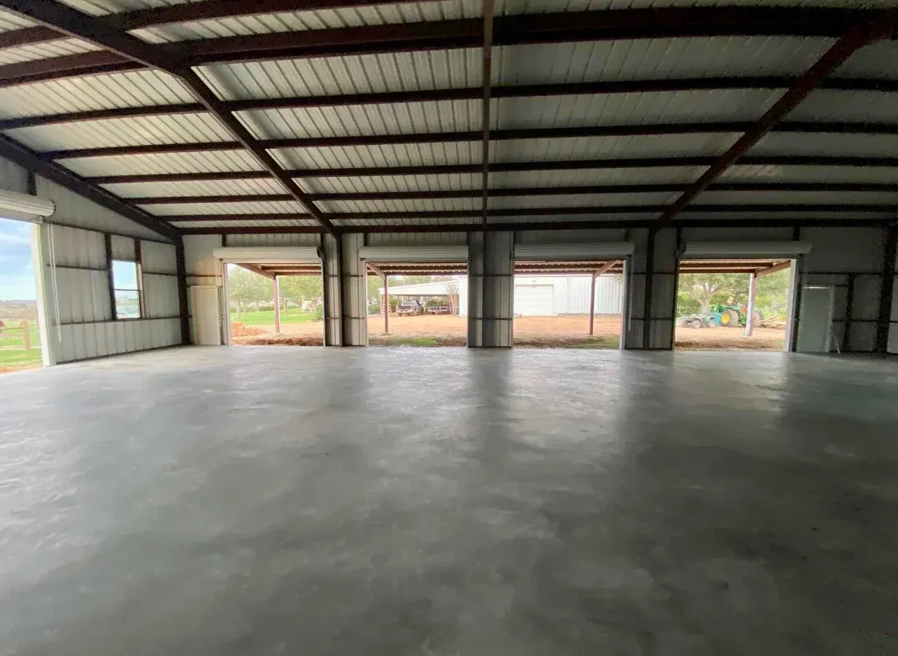 A large empty building with a concrete floor and a metal roof.