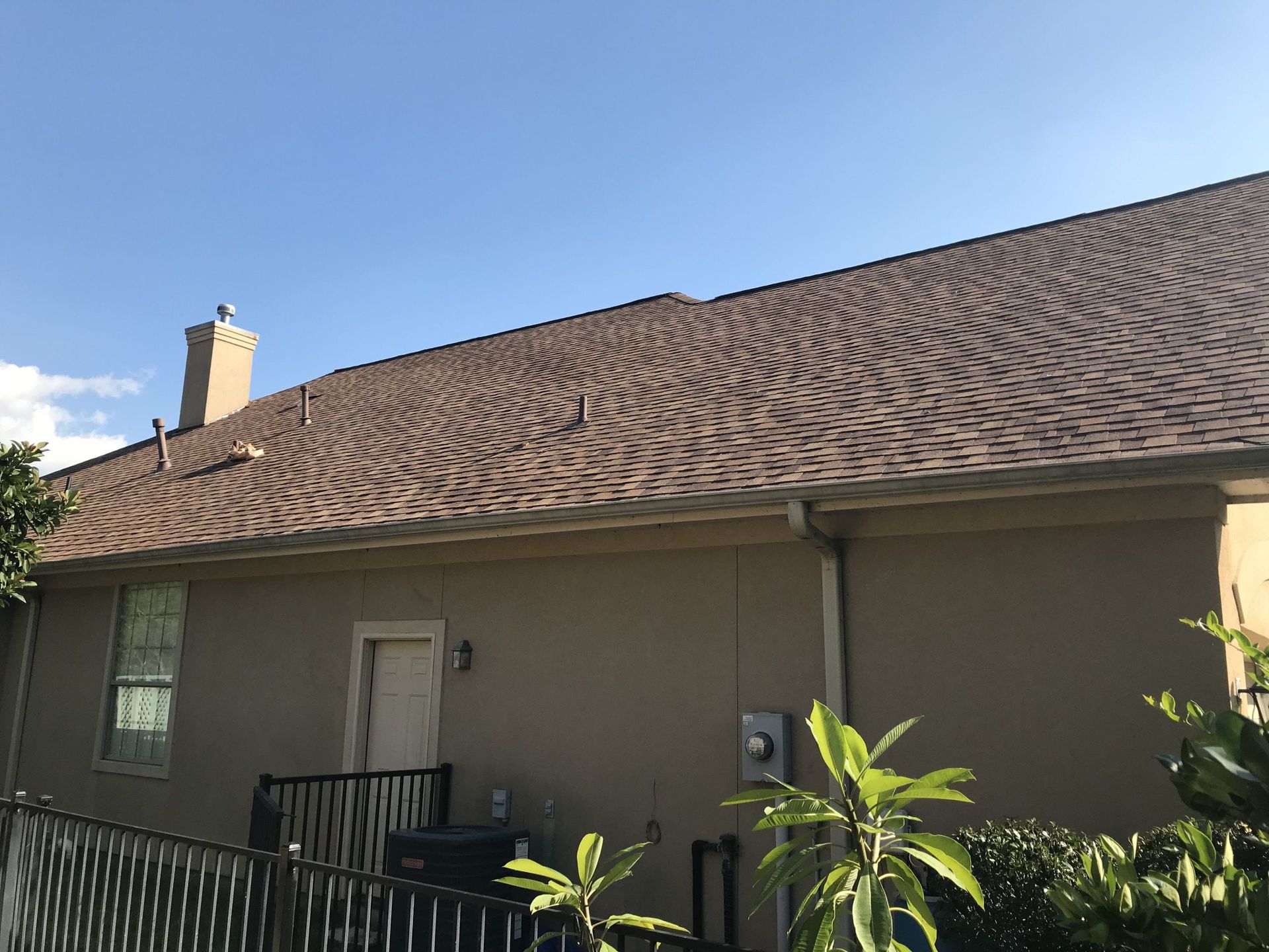 The back of a house with a brown roof and a chimney.