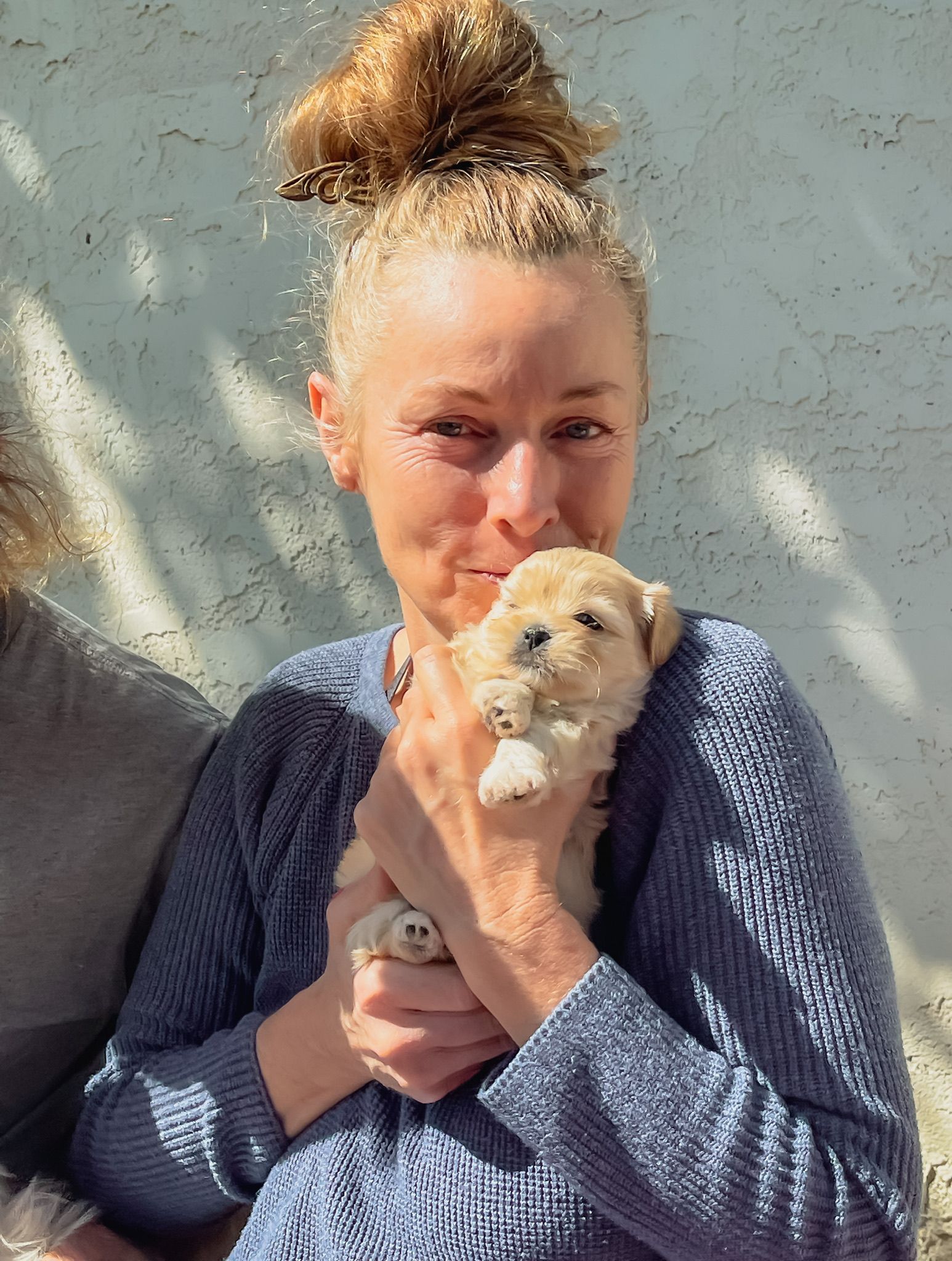 A woman in a blue sweater is holding a puppy in her arms.