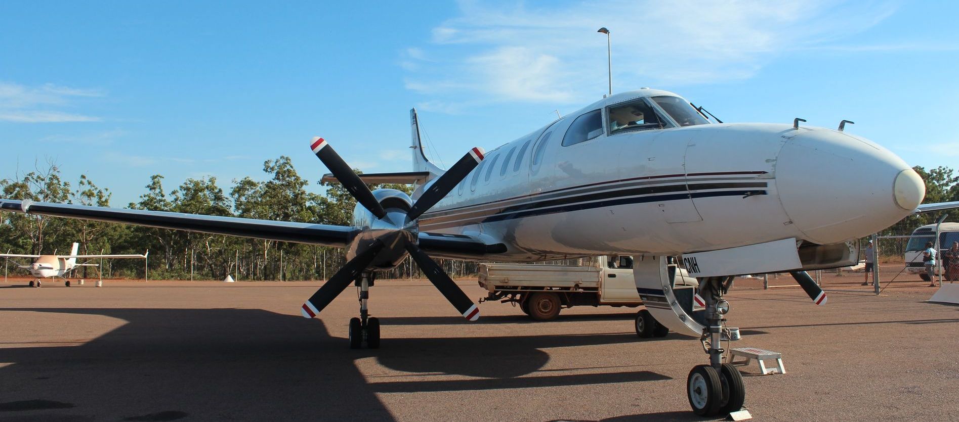 White and blue twin-engine airplane parked on an airfield with a blue sky in the background.