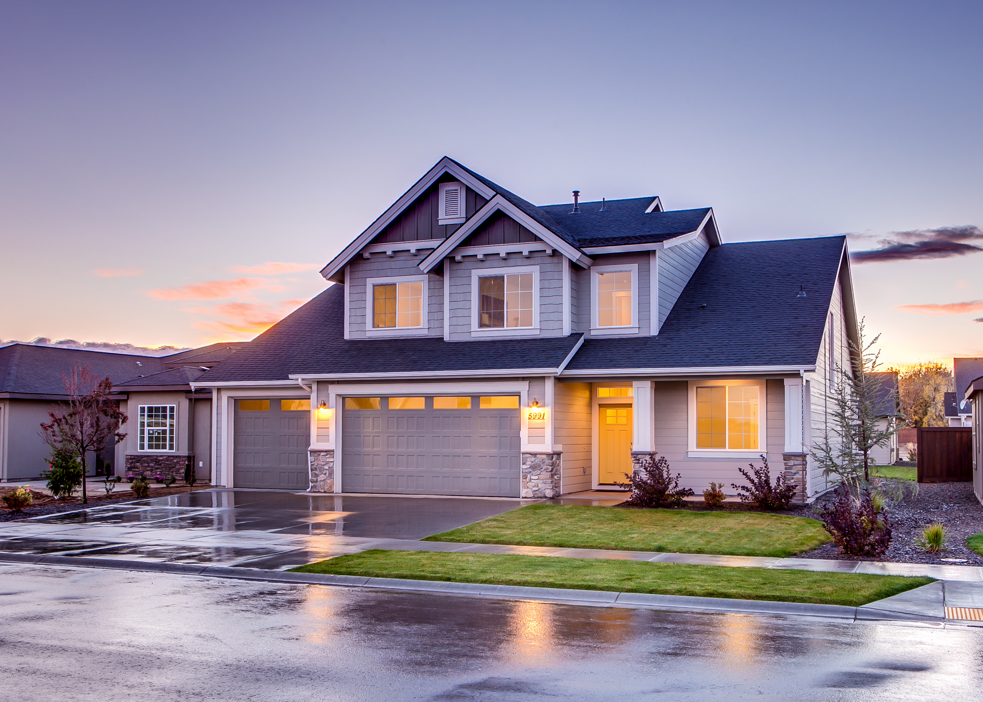 A large house with a garage and a driveway on a rainy day.