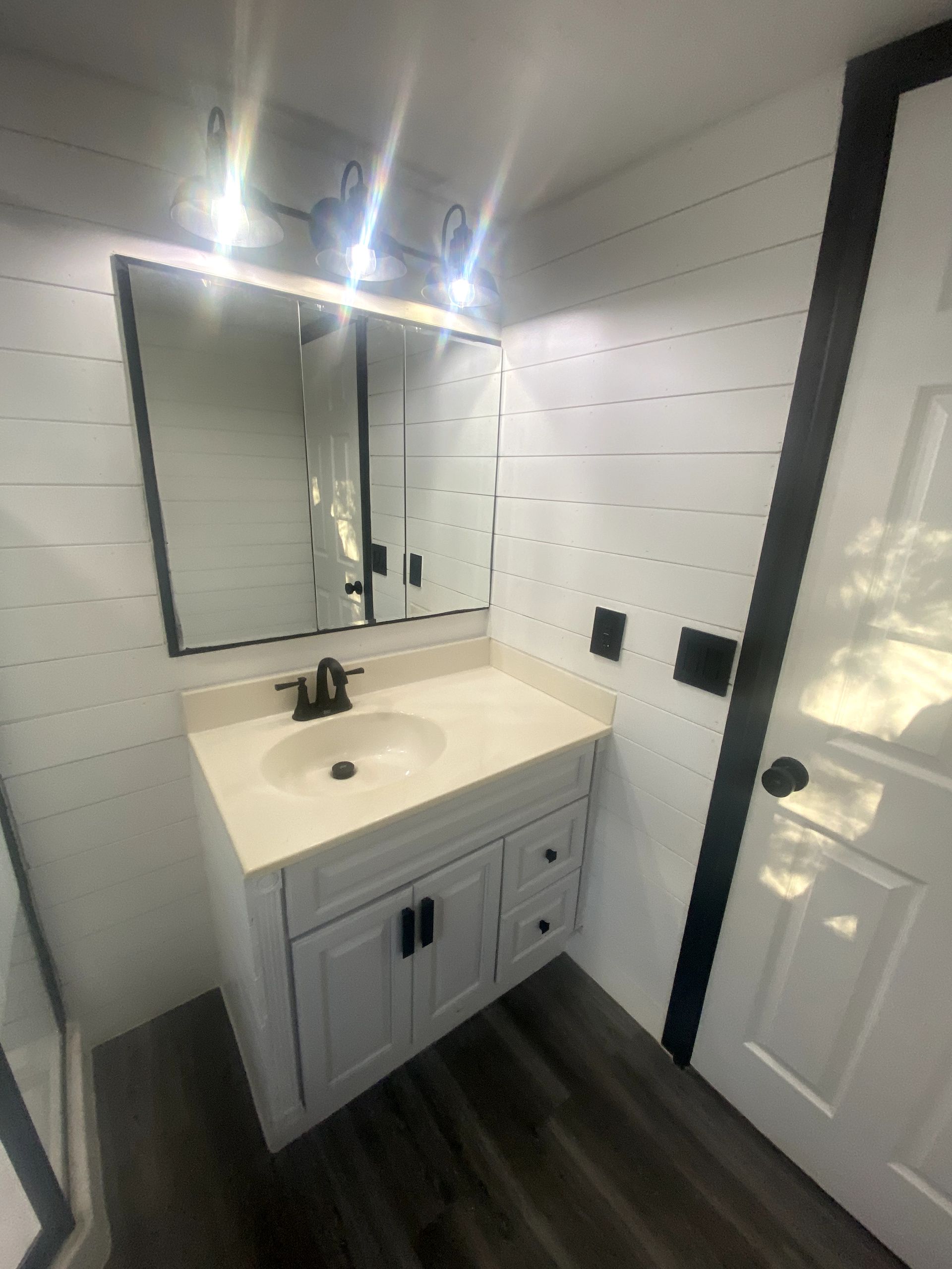 A bathroom with a sink , mirror and door.