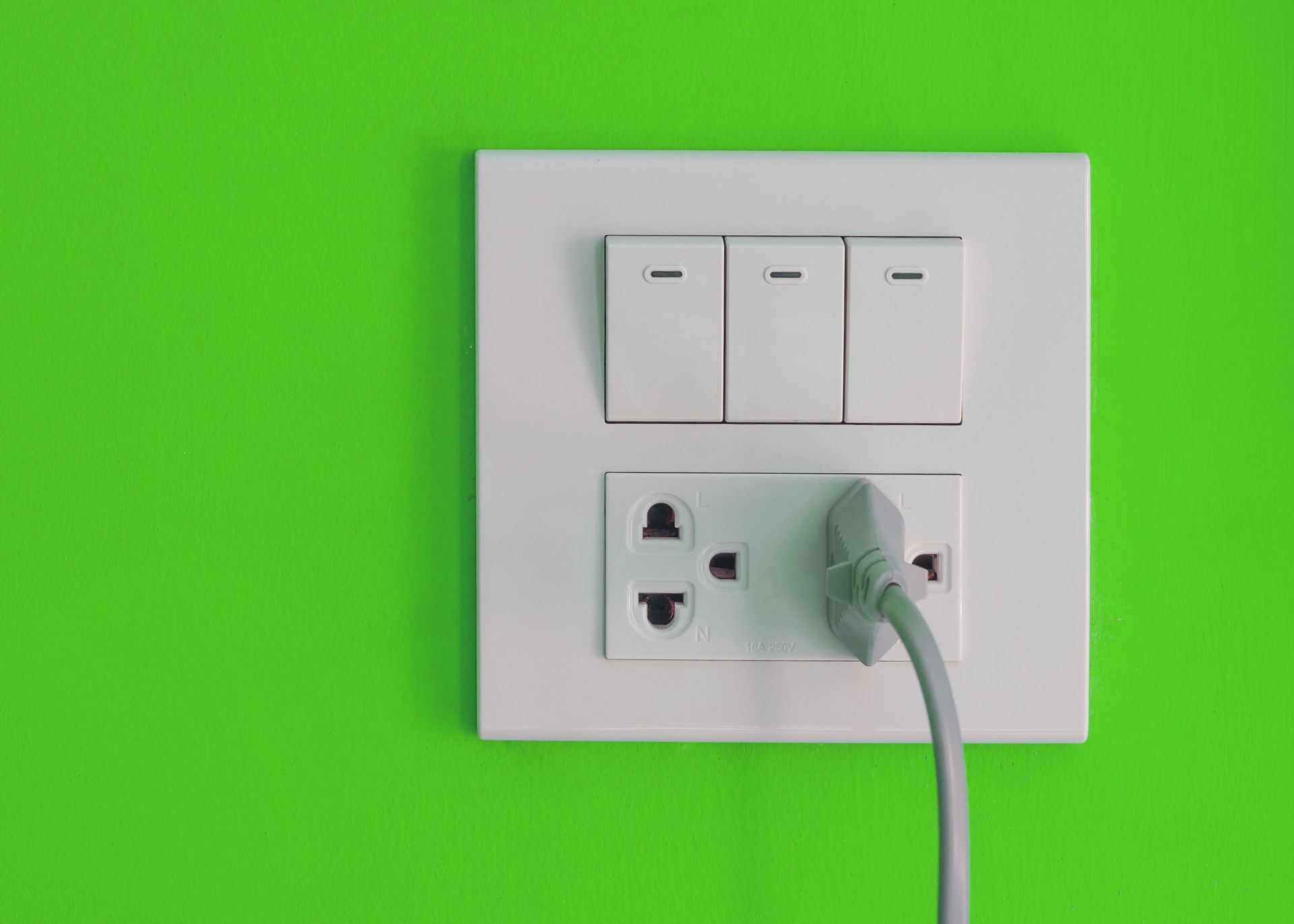 A plug is plugged into a light switch on a green wall.