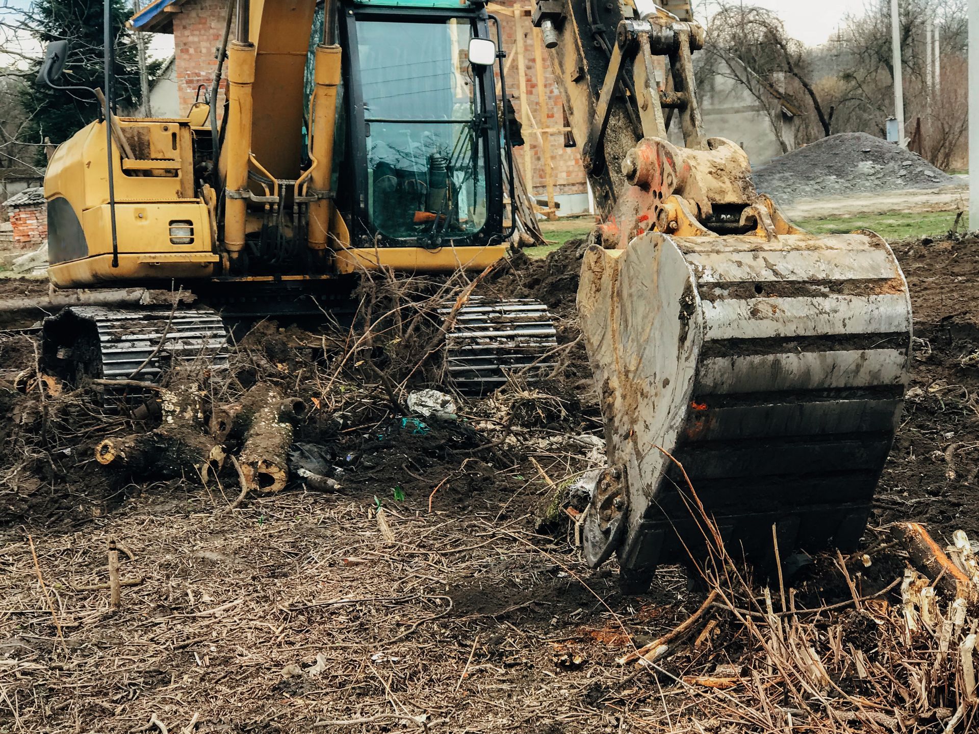 Excavator clearing countryside land by uprooting old trees, roots, branches, and debris.