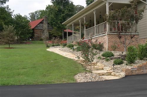 A house with a large porch and a log cabin in the background