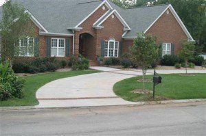 A large brick house with a concrete driveway and a mailbox in front of it.
