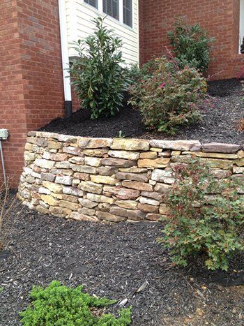 There is a stone wall in front of a brick house.