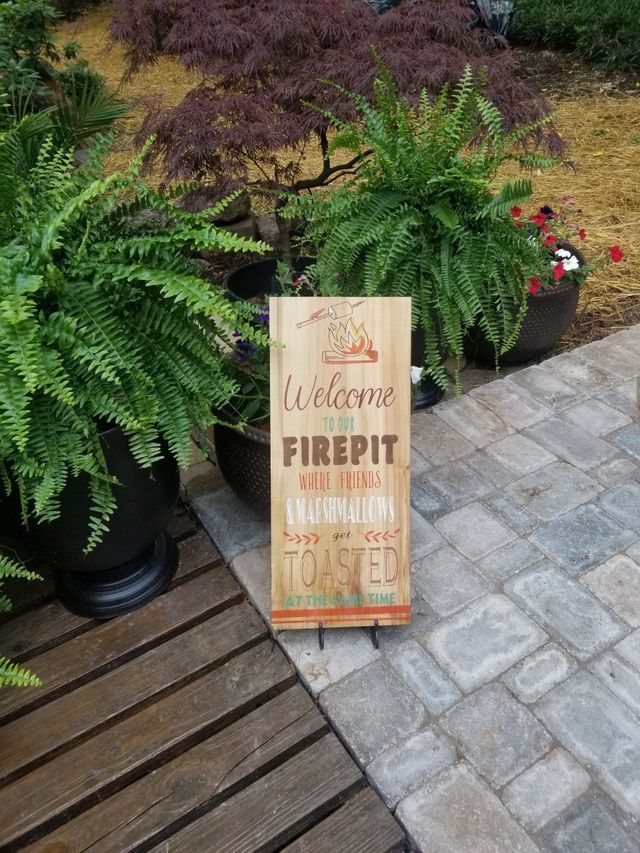 A wooden sign is sitting on a patio next to potted plants.