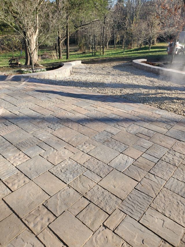A brick patio with a fountain in the background in a park.