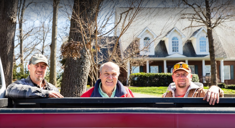 Three men are standing in the back of a truck.