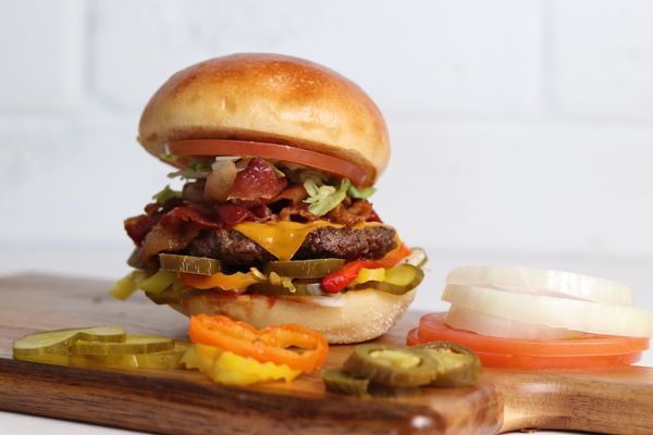 Delicious burger with toppings on a wooden board. Includes pickles, onions, and tomato slices.