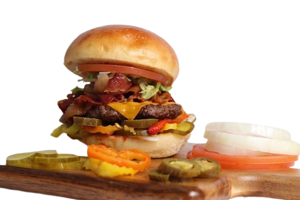 Cheeseburger with bacon, pickles, and toppings on a wooden board, with side of onion, tomato, and jalapeños.