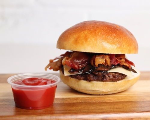 Hamburger on brioche bun with bacon, cheese, and a side of ketchup.