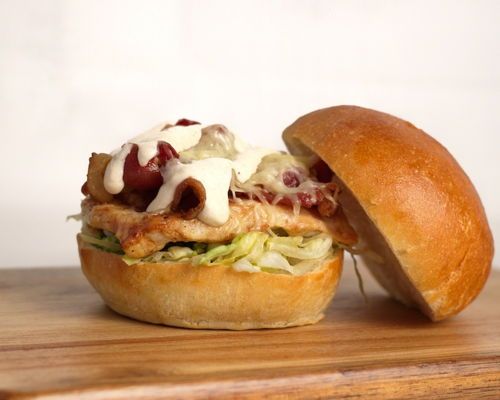 Chicken sandwich on a wooden board, with lettuce, sauce, and cheese.