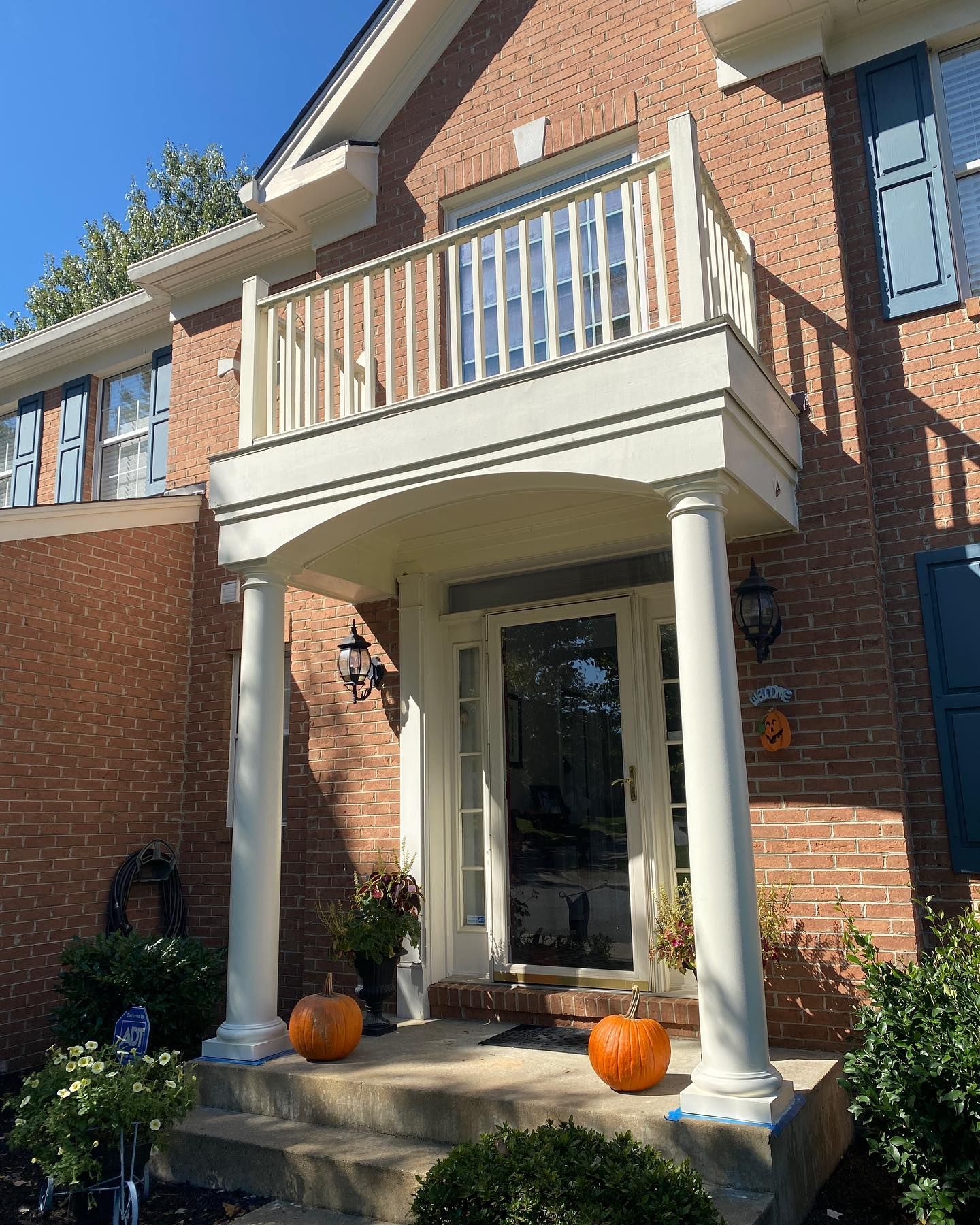 Red brick house with a front porch, balcony, pumpkins, and blue shutters.