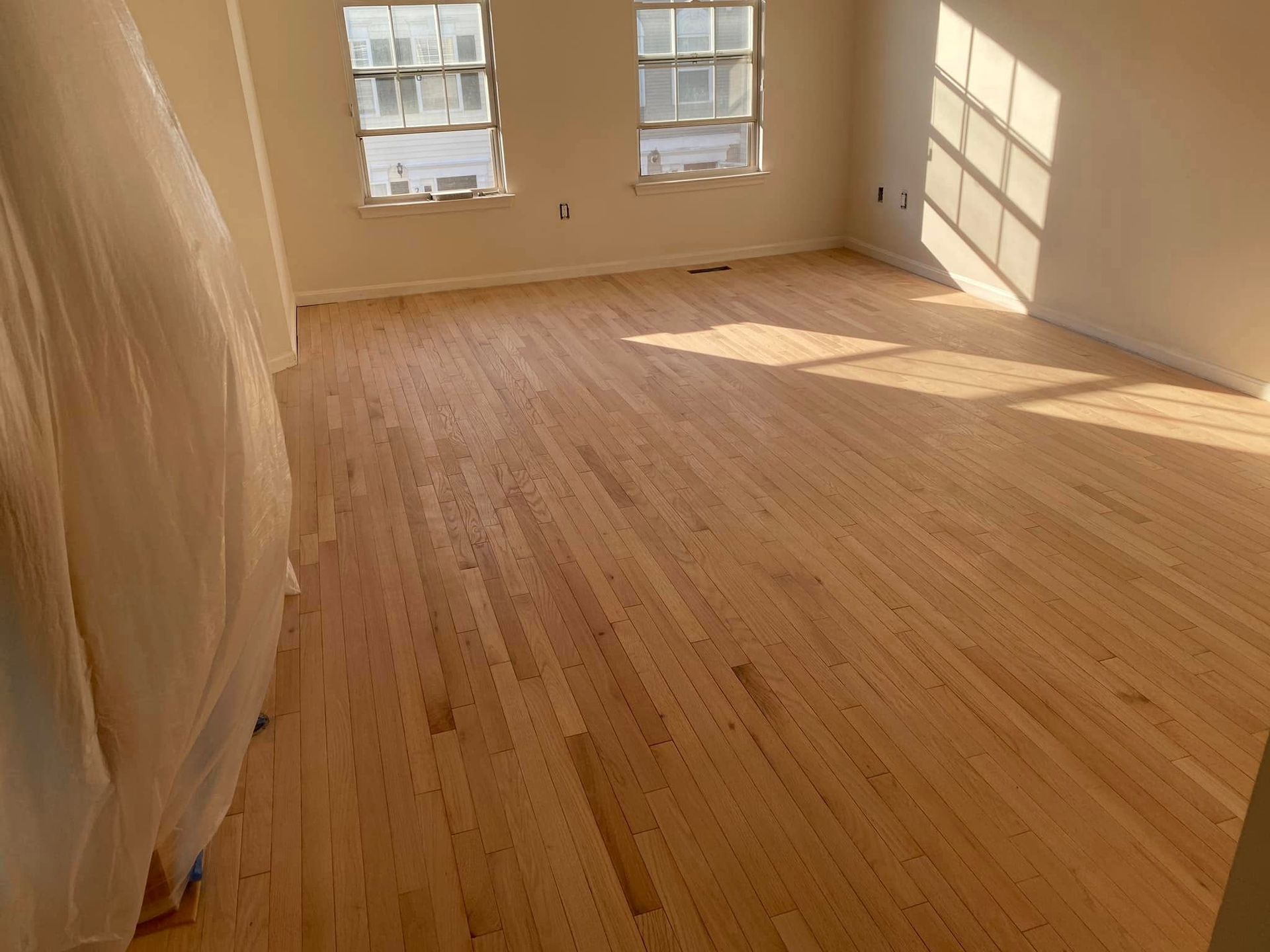 Newly installed, light wood floor in a sunlit room with two windows.