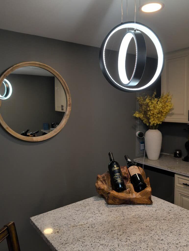 Kitchen with gray walls, round mirror, granite countertop, wine bottles in wooden holder, and a circular pendant light.