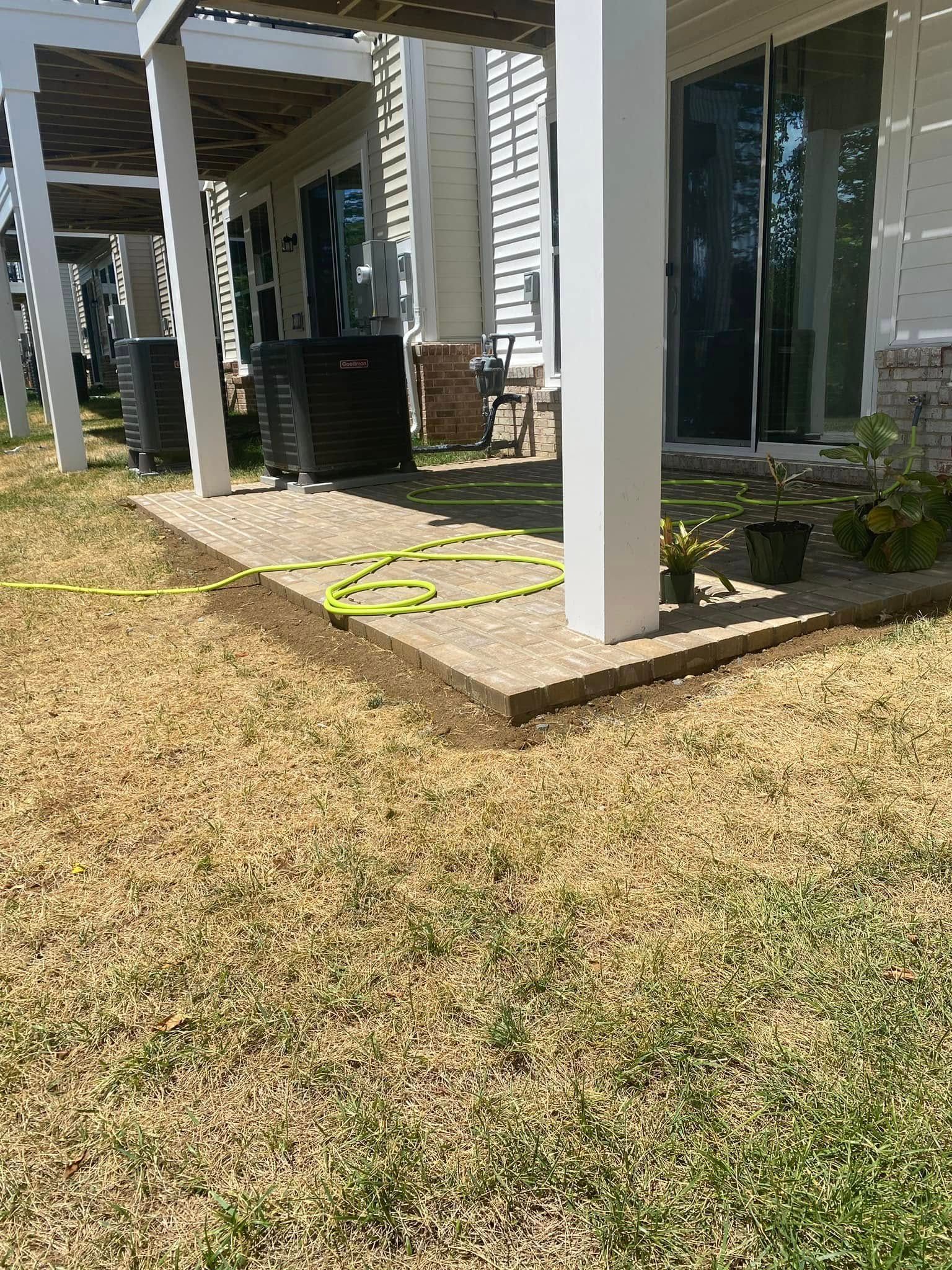 Patio area with brown grass, air conditioning units, and a coiled green hose.