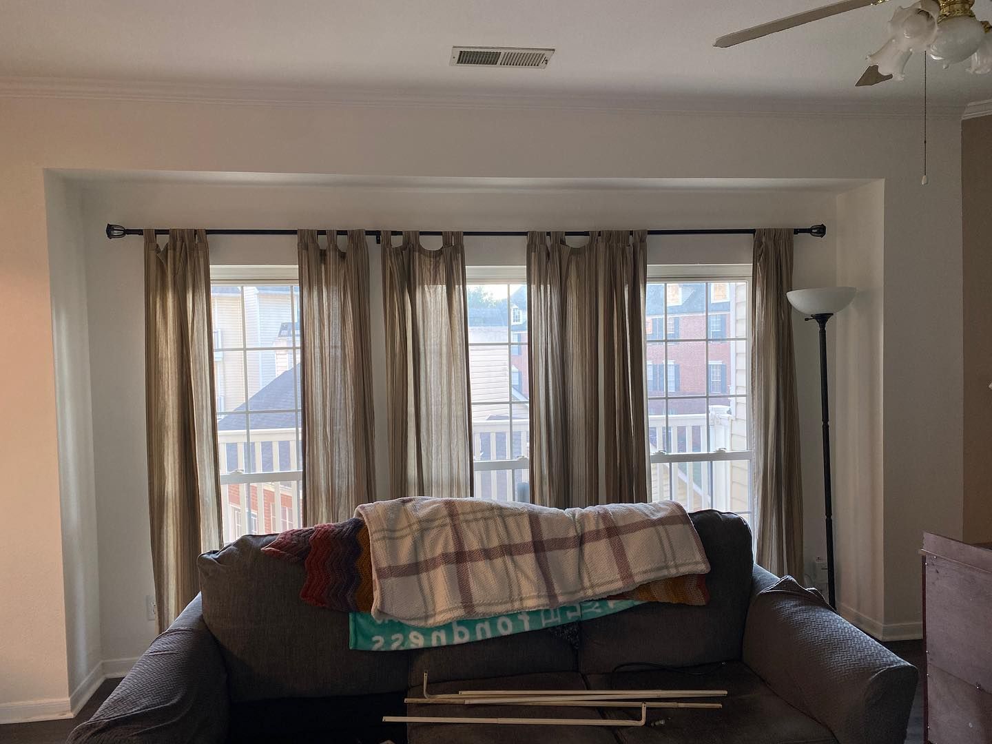 Living room with couch, curtains, and windows. Brown curtains, gray couch, and neutral-colored walls.