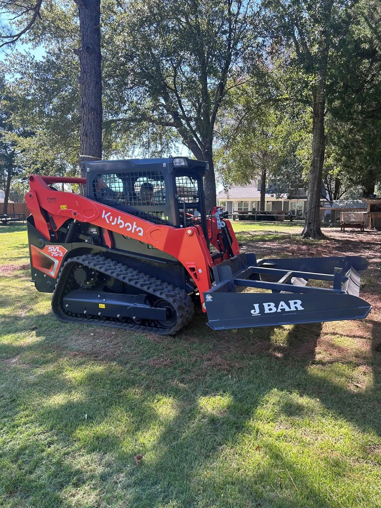 Orange Kubota track loader with a J BAR grapple attachment on grass.