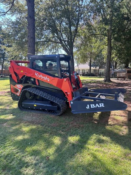Orange Kubota track loader with J Bar attachment on a grassy lawn.