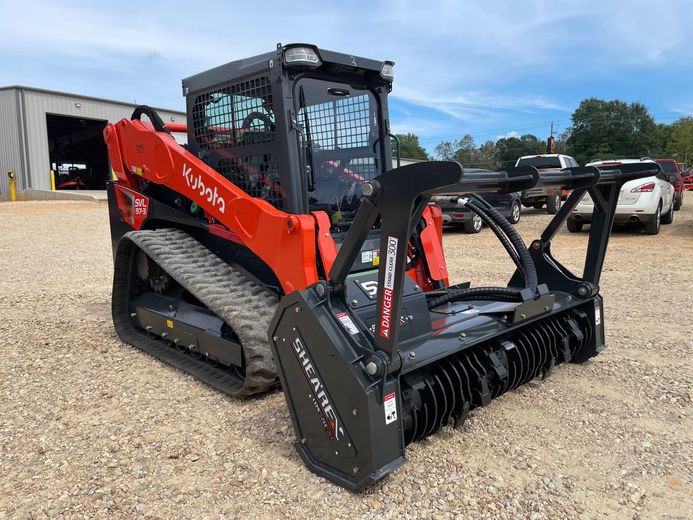 Orange Kubota track loader with black brush cutter attachment, on gravel.
