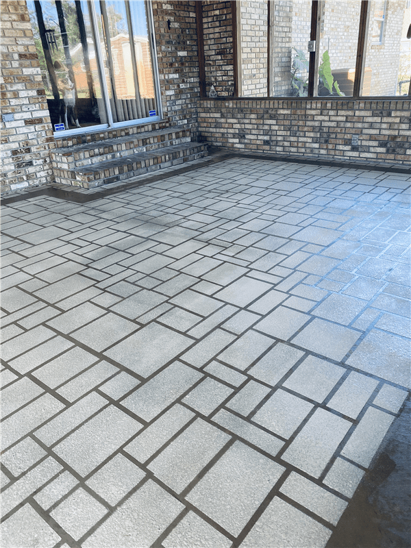Brick patio with a rectangular pattern, adjacent to a brick and glass building.