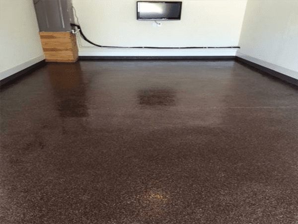 Brown speckled epoxy garage floor. TV mounted on white wall, wooden cabinet. Black trim.