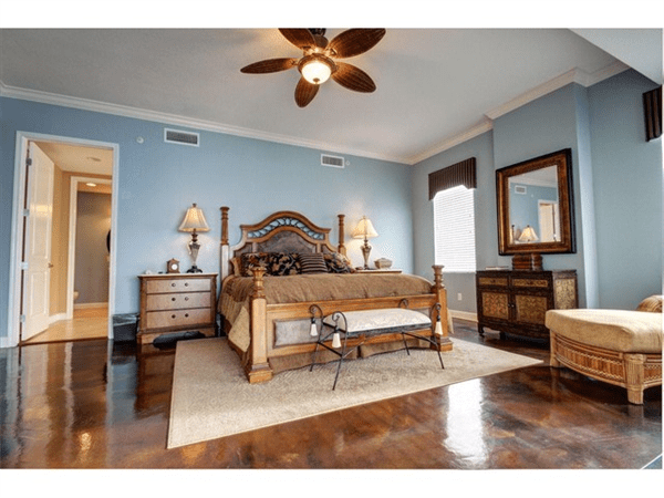 Elegant bedroom with a four-poster bed, wood furniture, and blue walls. Features a ceiling fan and a view to the hallway.