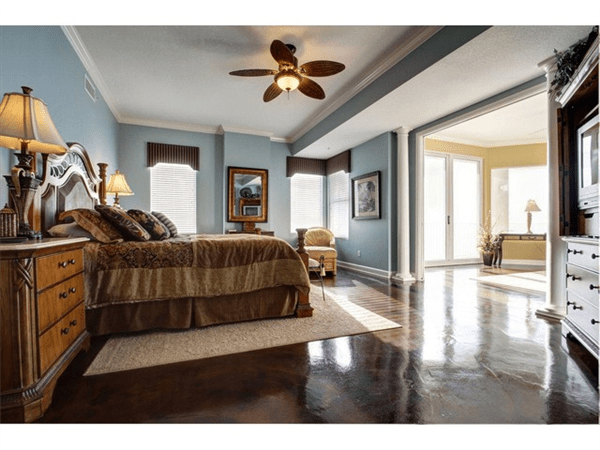 Spacious bedroom with blue walls, dark floors, ornate bed, and access to a sunlit balcony.