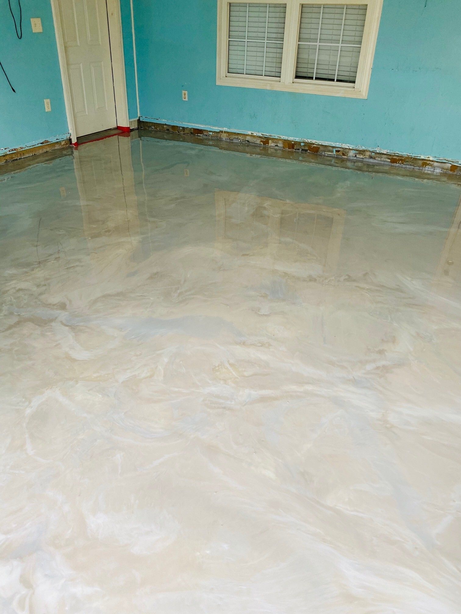 Room with epoxy flooring. The floor is light-colored and swirled. Blue walls, a white door, and window are visible.