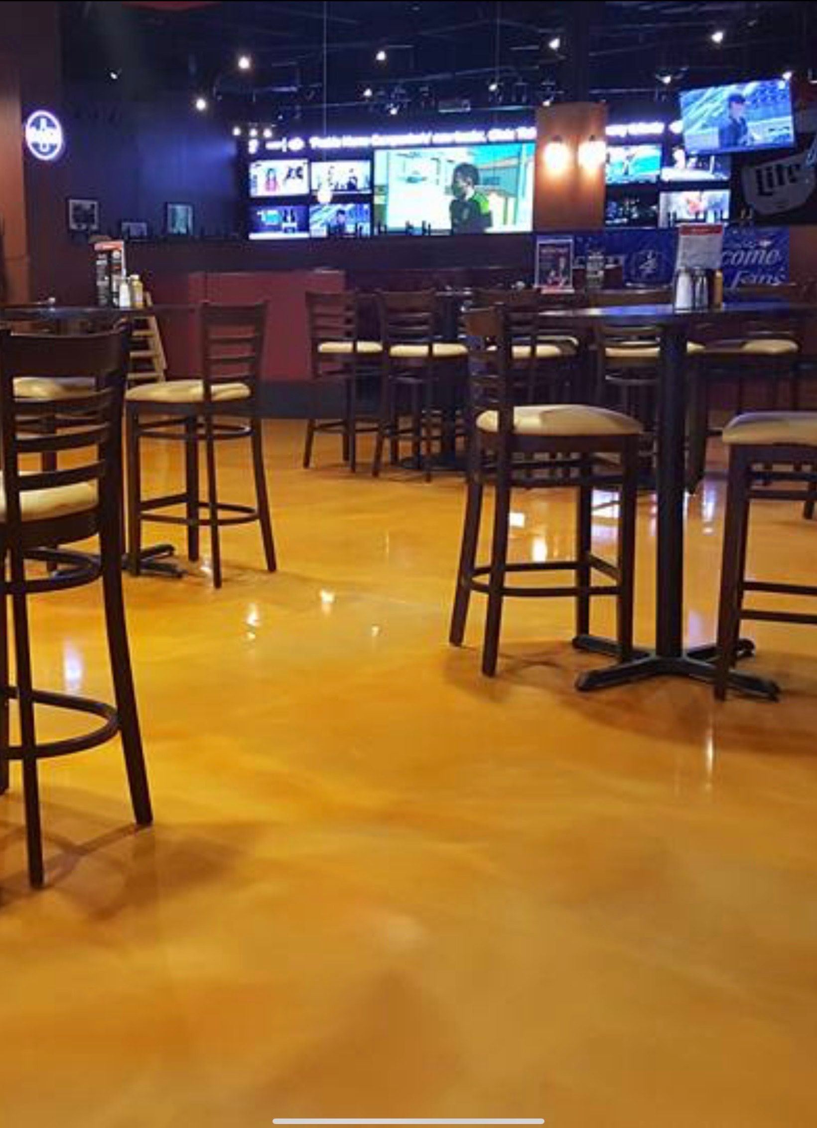 Interior of a bar with tables, chairs, and large TVs. Golden floor reflects light.
