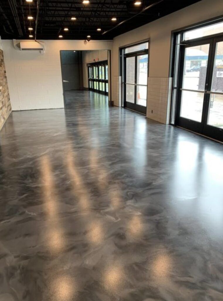 Empty room with polished metallic gray floor, large windows, and recessed lighting.
