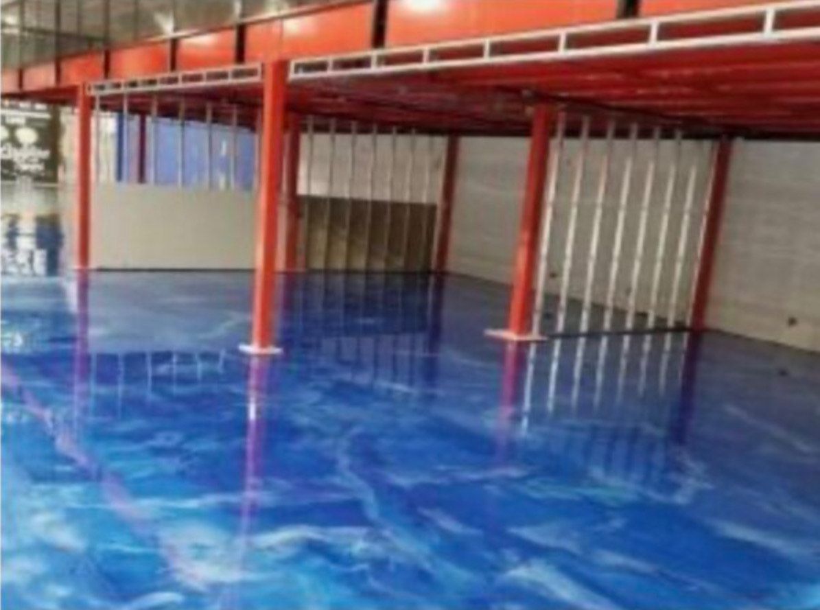 Blue epoxy floor beneath a red metal structure, reflecting the beams and pillars.