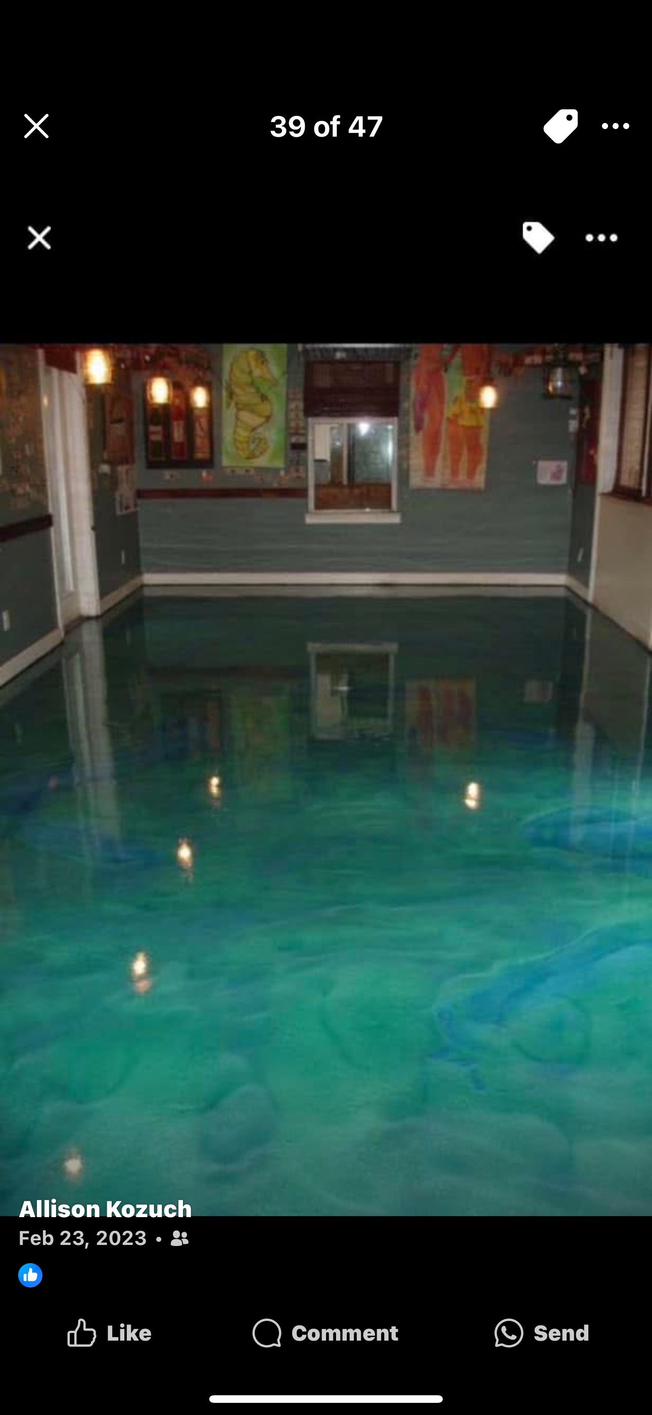 A room with a shiny, turquoise-colored epoxy floor. The walls are a dark grey, with abstract art. A room with a shiny, turquoise-colored epoxy floor. The walls are a dark grey, with abstract art.