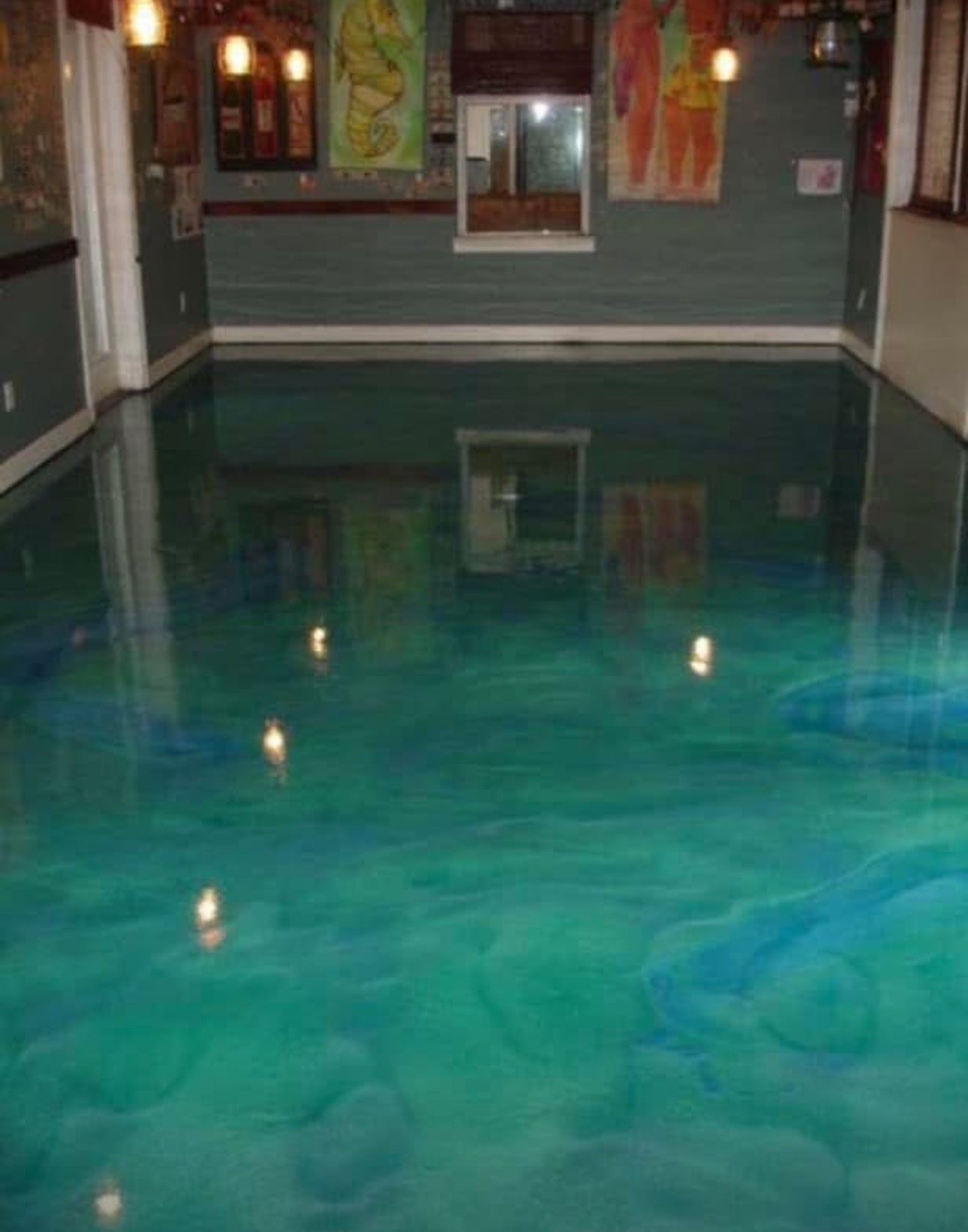 A room with a shiny, turquoise-colored epoxy floor. The walls are a dark grey, with abstract art.