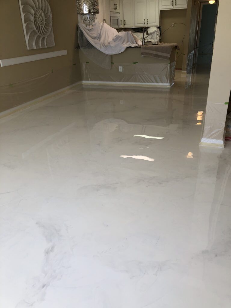 White epoxy floor in a room, reflecting light. Kitchen island in the background, art on the wall.