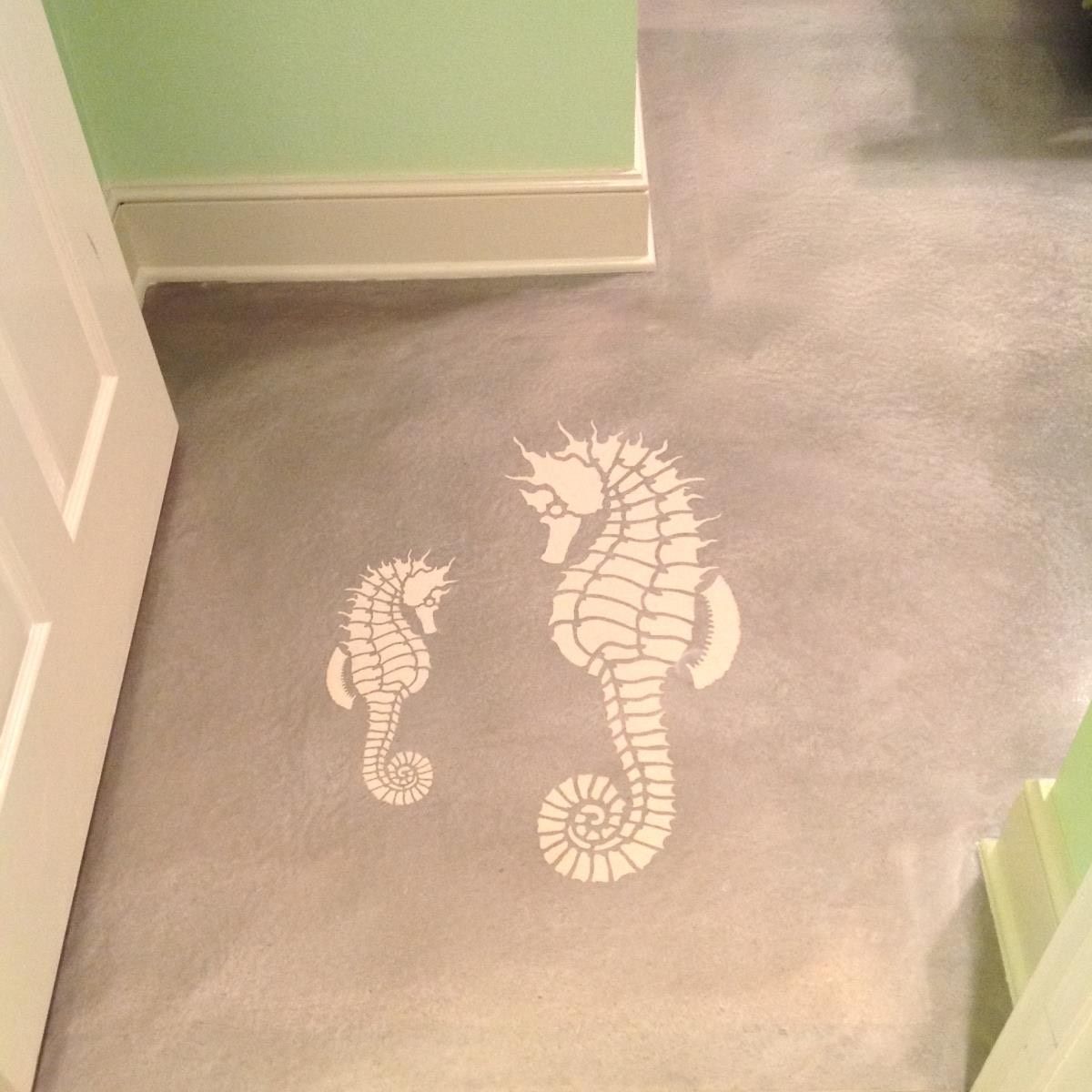 Two seahorse stencils on a gray painted floor. Green and white walls are in view.