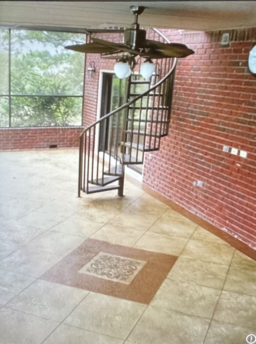 Indoor space with spiral staircase, brick walls, and tan tile floor. Ceiling fan.