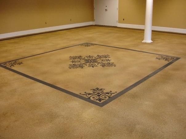 Brown concrete floor with a black square border and ornate center design. Beige walls and white column.